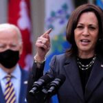 Woman speaking at podium, man with mask behind.