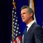 California Governor Newsom Proposes Doubling Film Tax Credits to Boost Economic Growth and Innovation Man in suit speaking, flanked by American flags.