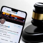Smartphone displaying Twitter profile near a judge's gavel.