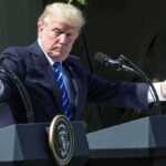 Man gesturing at two podiums outdoors.