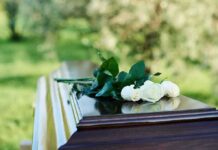 People placing white roses on a casket.