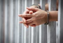 Hands in handcuffs gripping prison bars