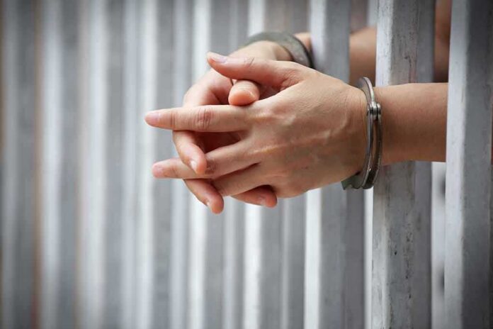 Hands in handcuffs gripping prison bars