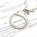 Handcuffs on top of an arrest warrant document.