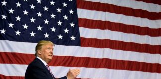 Man clapping in front of American flag backdrop