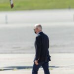Person walking on tarmac wearing a black mask.
