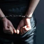 Hands in handcuffs behind back in dark room.