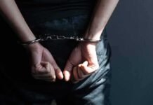 Hands in handcuffs behind back in dark room.
