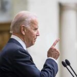 Man in suit pointing while speaking at podium.