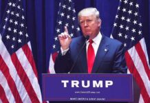 Person speaking at podium with American flags behind