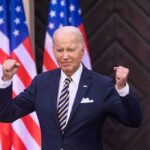 Man in suit raising fists American flags behind him