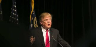 Man speaking at podium with flags in background