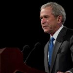 A man speaking at a podium in a dark room.