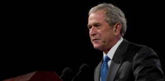 A man speaking at a podium in a dark room.