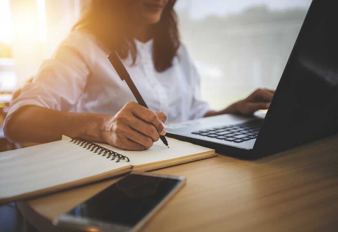 1207740871 featured image Person writing in notebook using laptop nearby