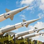 Multiple missiles pointed upward on launchers against blue sky