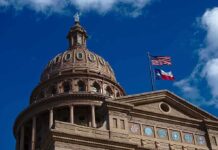 Building dome with US and Texas flags blue sky
