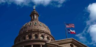 Building dome with US and Texas flags blue sky