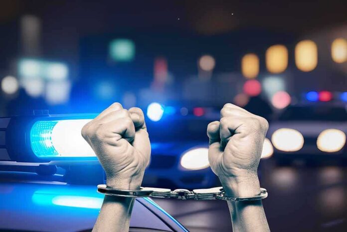 Handcuffed hands raised police cars with lights on