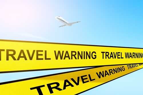 TRAVEL ADVISORY WARNING_2086996915.jpg featured image Airplane flying above travel warning signs sky background