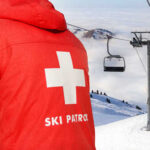 Ski patrol member near ski lift and snowy mountains