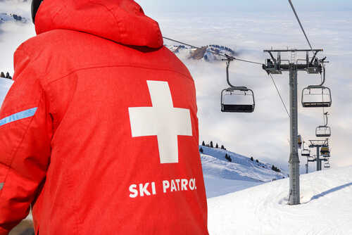 ski patrol_1810008562 featured image Ski patrol member near ski lift and snowy mountains