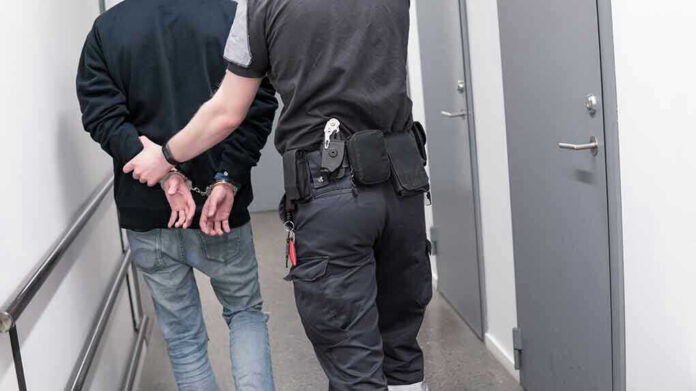1082126789 Officer escorting handcuffed person down hallway