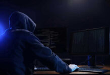 Hooded figure using dual monitors in dark room