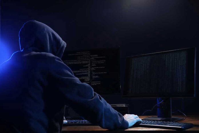 1708895812 Hooded figure using dual monitors in dark room