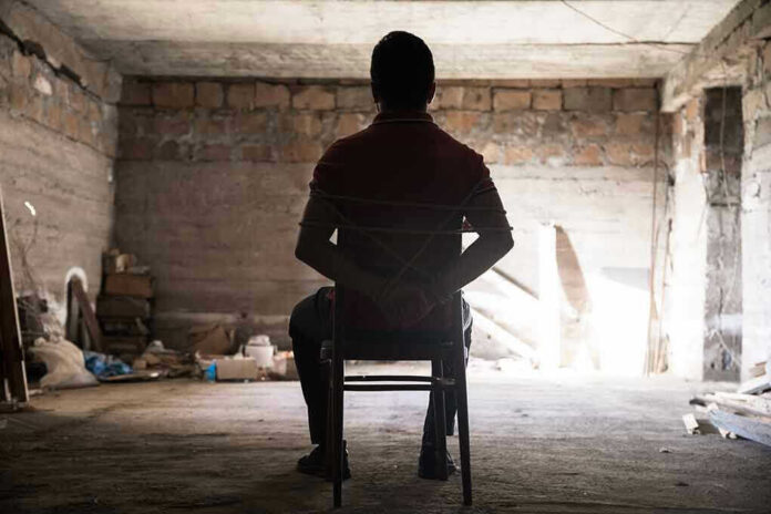 1784023241 Person tied to chair in dimly lit room.