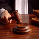 A judge's hand holding a gavel over a wooden desk with law books