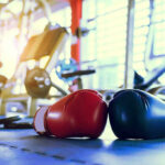 Boxing gloves on gym floor with equipment.