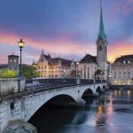 Scenic view of Zurich with a bridge, historic buildings, and a sunset sky
