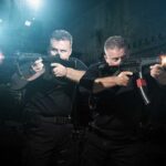Two tactical operators aiming firearms in a dimly lit urban setting