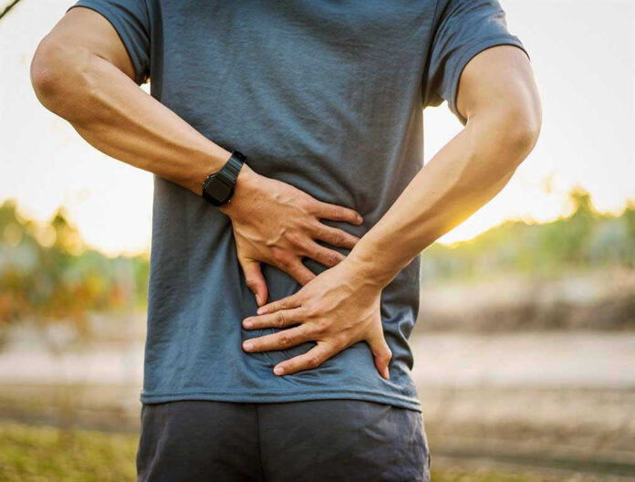 Person holding lower back in discomfort outdoors