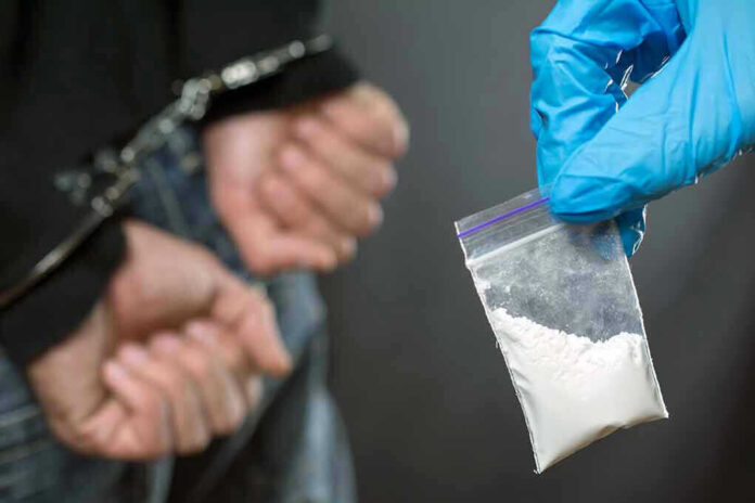 Person handcuffed, police holding bag of white substance.