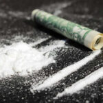 Powder lines, rolled dollar bill on black surface.