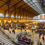Interior view of a busy train station with large windows and a staircase