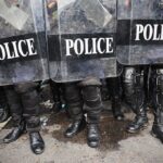 Police officers in riot gear standing behind shields marked POLICE