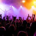 Crowd at a concert with raised hands and colorful stage lights