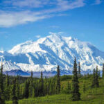 Snow-covered mountain under blue sky with green foreground