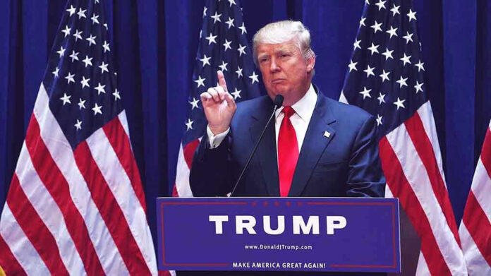 Man speaking at podium with USA flags behind him