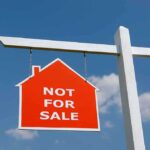 Red Not For Sale sign hanging from a white post against a blue sky
