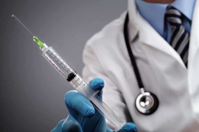 A doctor holding a syringe with a stethoscope around their neck
