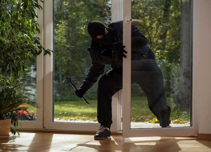 A burglar in dark clothing entering a house through a glass door