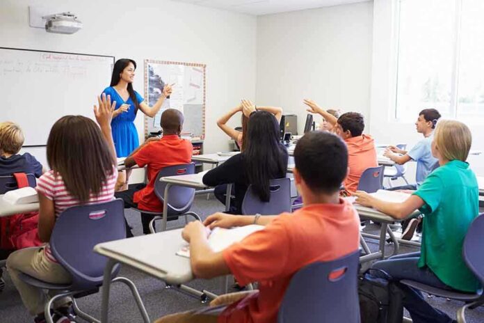 Teacher in a blue dress instructing students in a classroom with hands raised