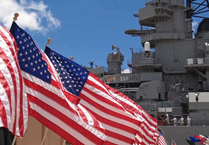 American flags in front of a naval ship under a blue sky