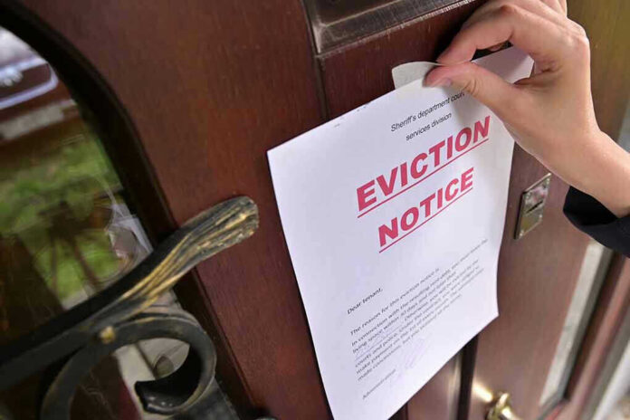 Hand tacking eviction notice on a wooden door.