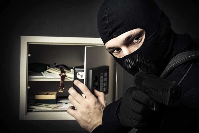 A masked burglar holding a gun while attempting to open a safe