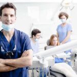 A dentist smiling in a dental office with a team assisting a patient